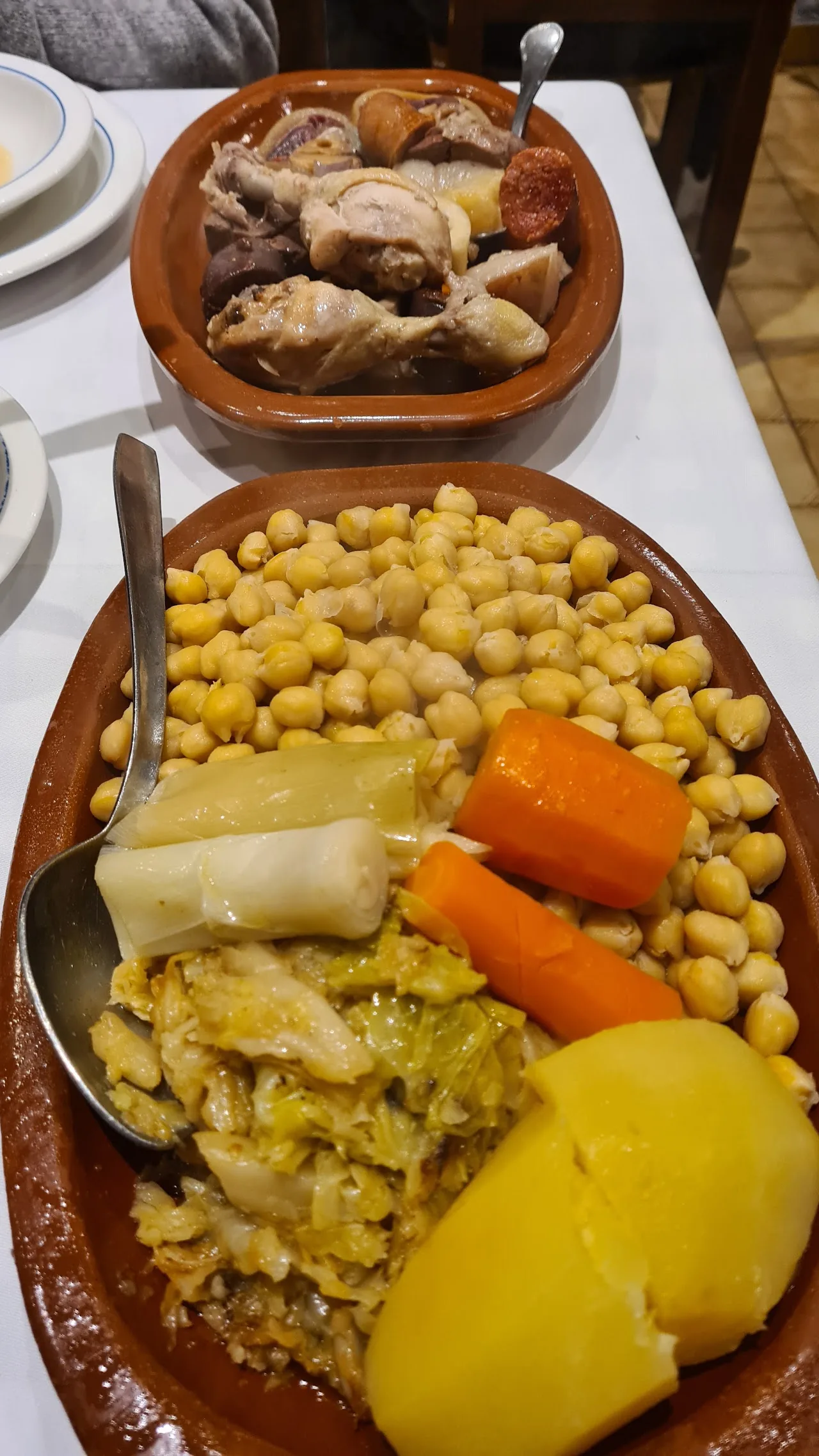 A clay dish of cocido madrileño with chickpeas, meat, carrots, and potato