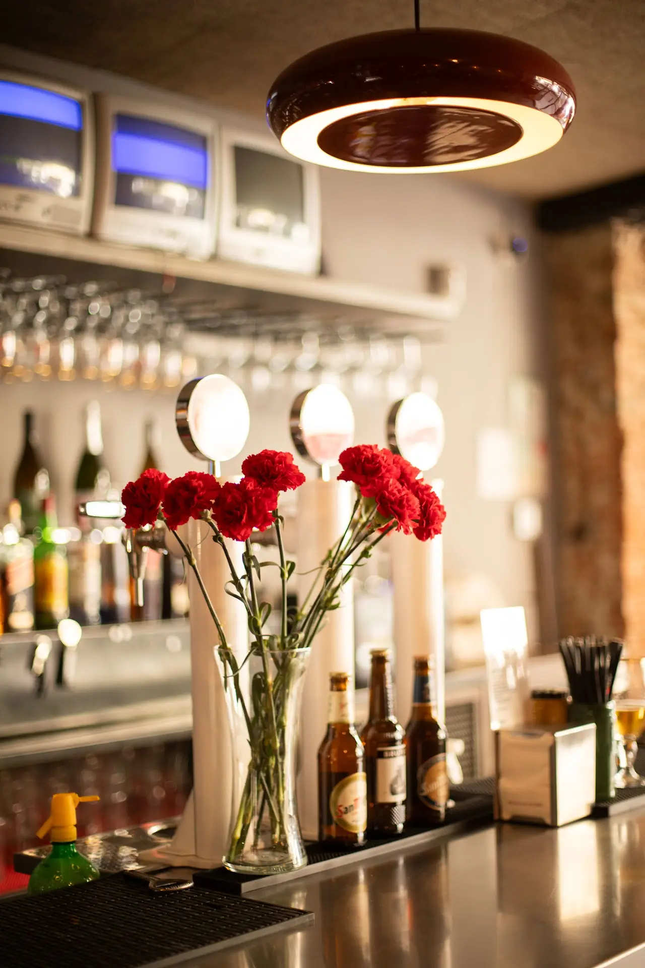 Bar counter with a vase of red carnations and bottles lined up along the back bar.