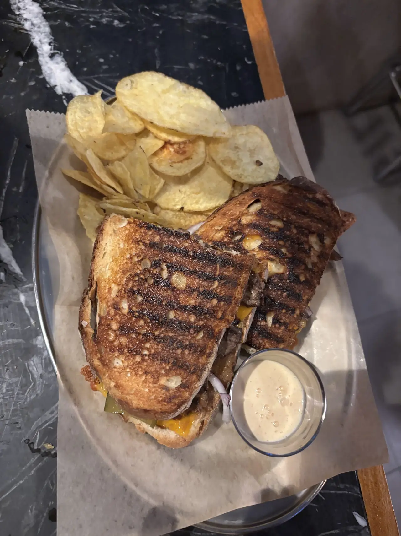 A grilled pressed sandwich cut in half, served with potato chips and a dip.