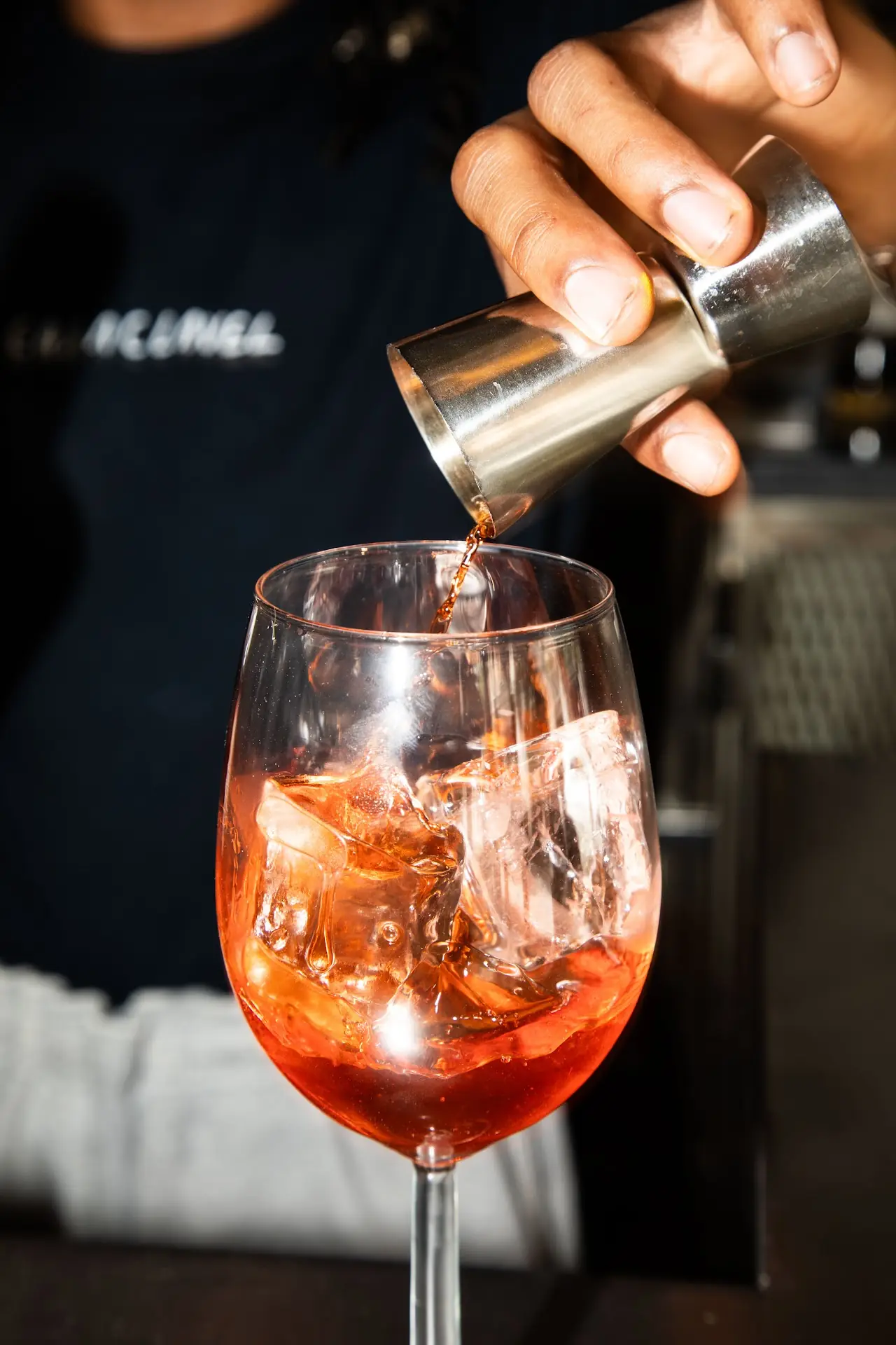 A hand pouring a garnish into an orange spritz cocktail with ice.