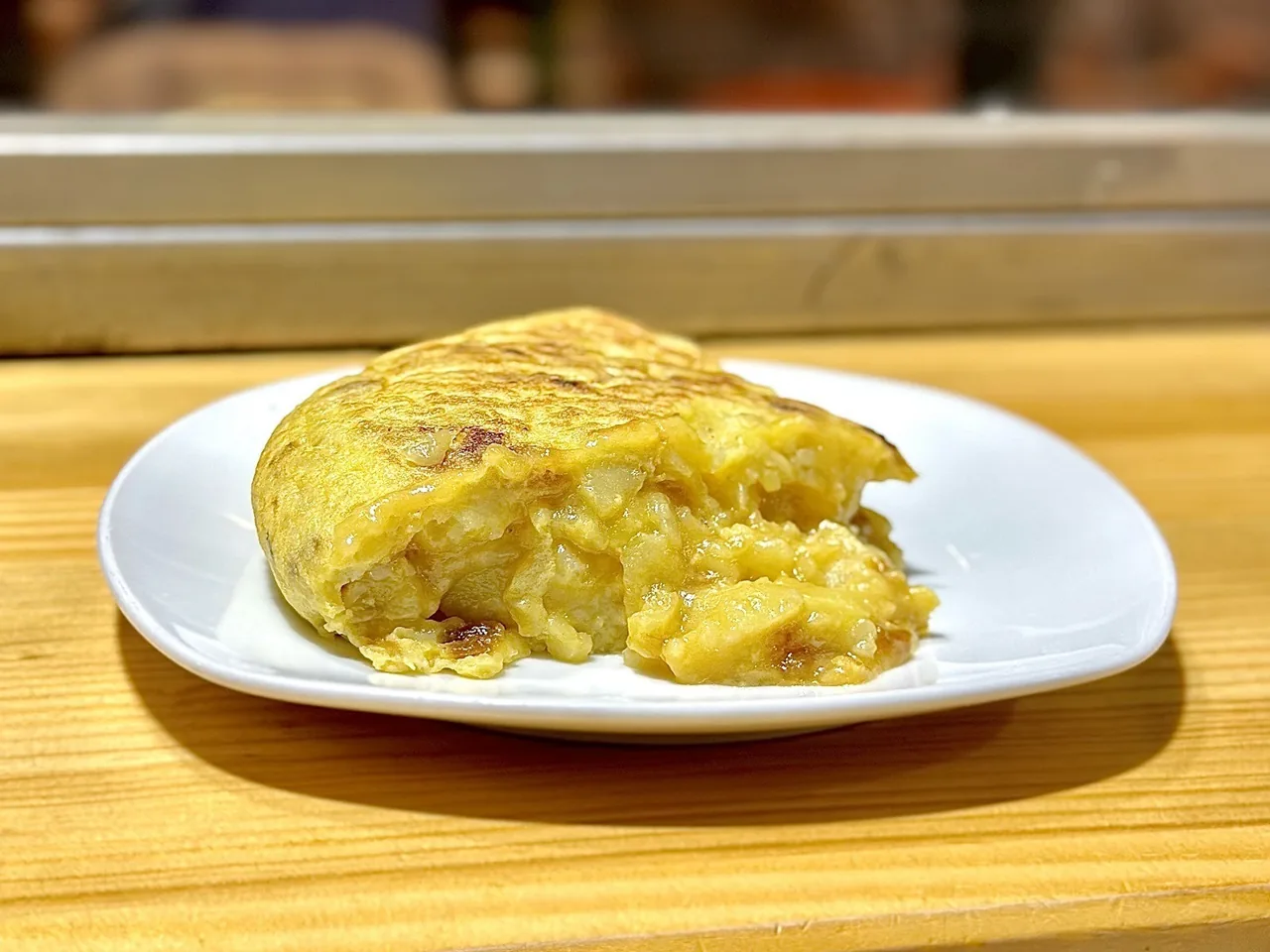 A wedge of tortilla de patata with a soft centre on a white plate on a wooden counter