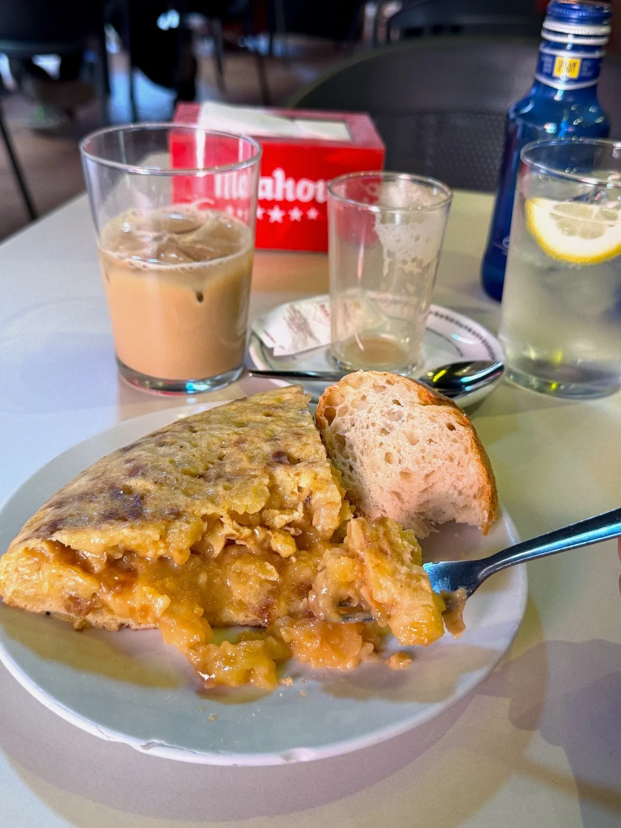 A slice of tortilla on a plate next to a glass of iced coffee on a table