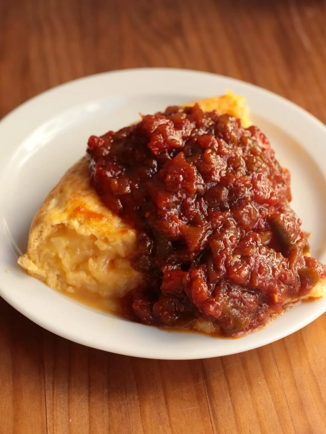 A wedge of tortilla topped with a dark red meat sauce on a white plate