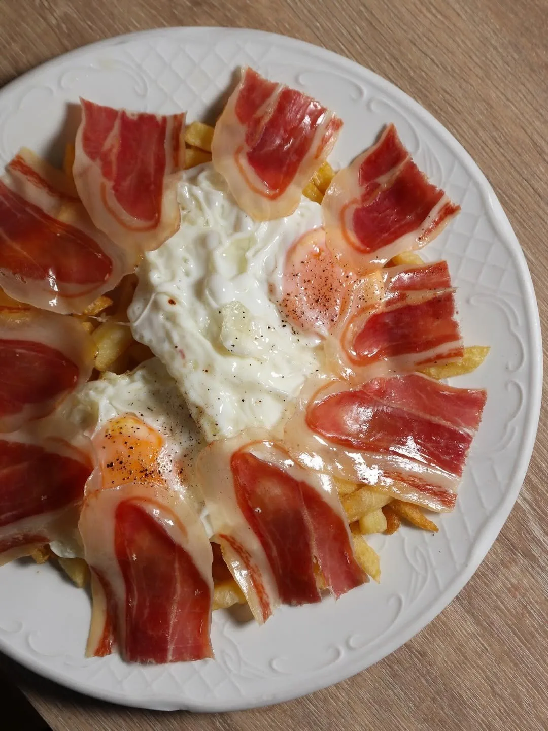 A white plate of sliced cured ham over a soft white topping on fried potatoes