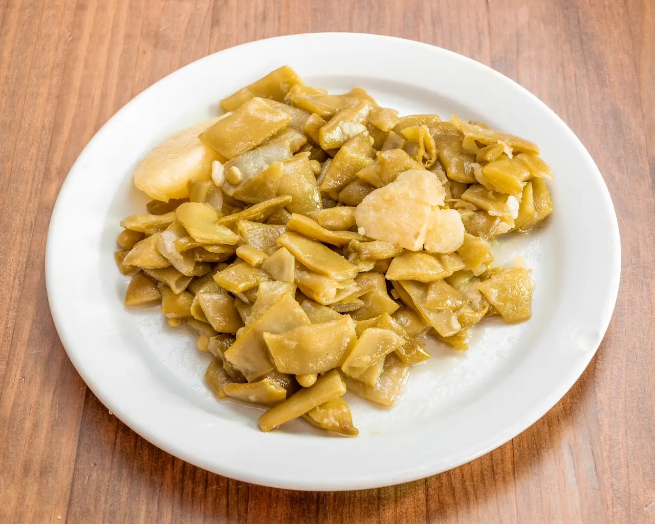 Plate of sliced sauteed green beans with pieces of potato and pine nuts