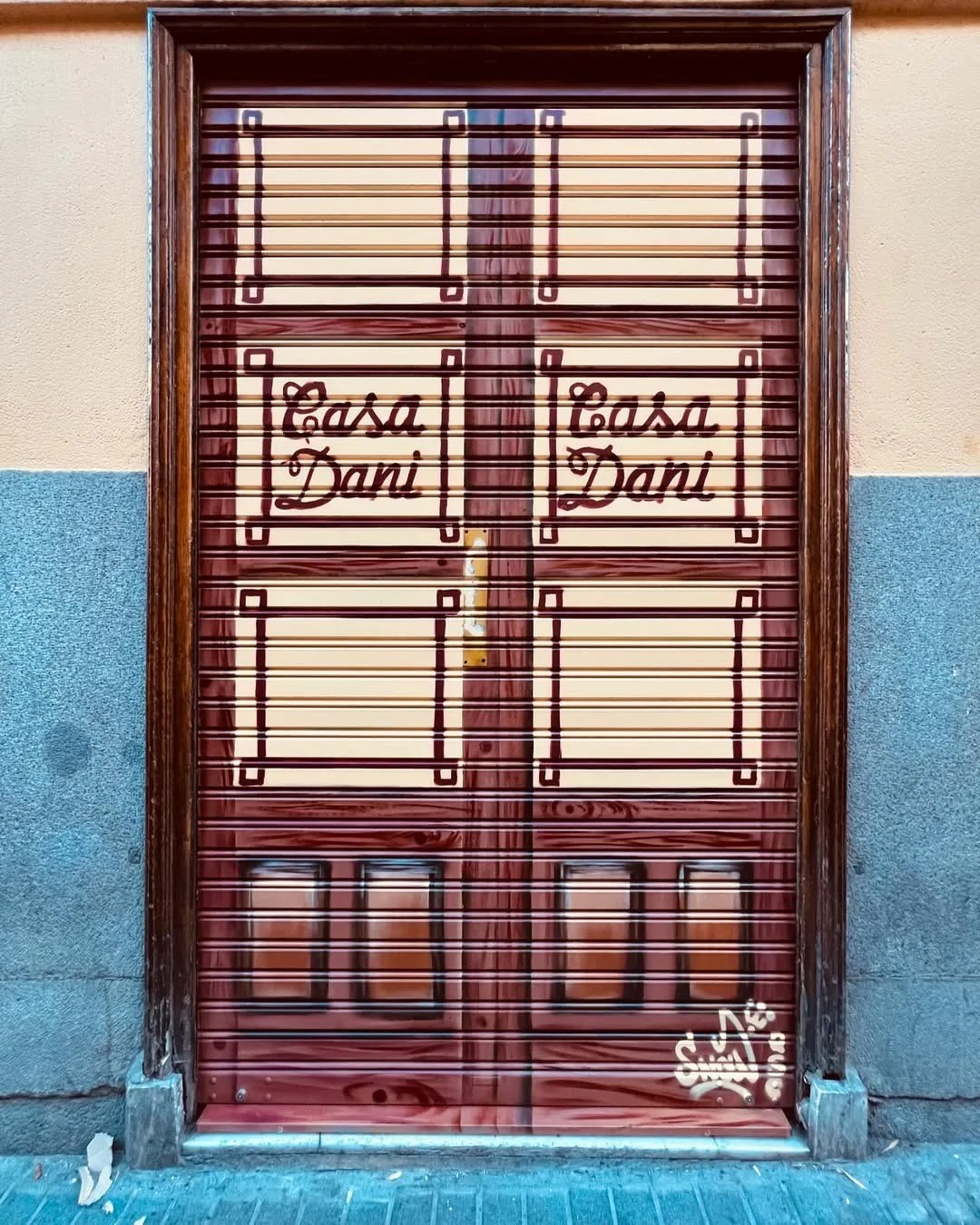 A wooden double door with lettering on the glass panels above a blue-tiled wall.