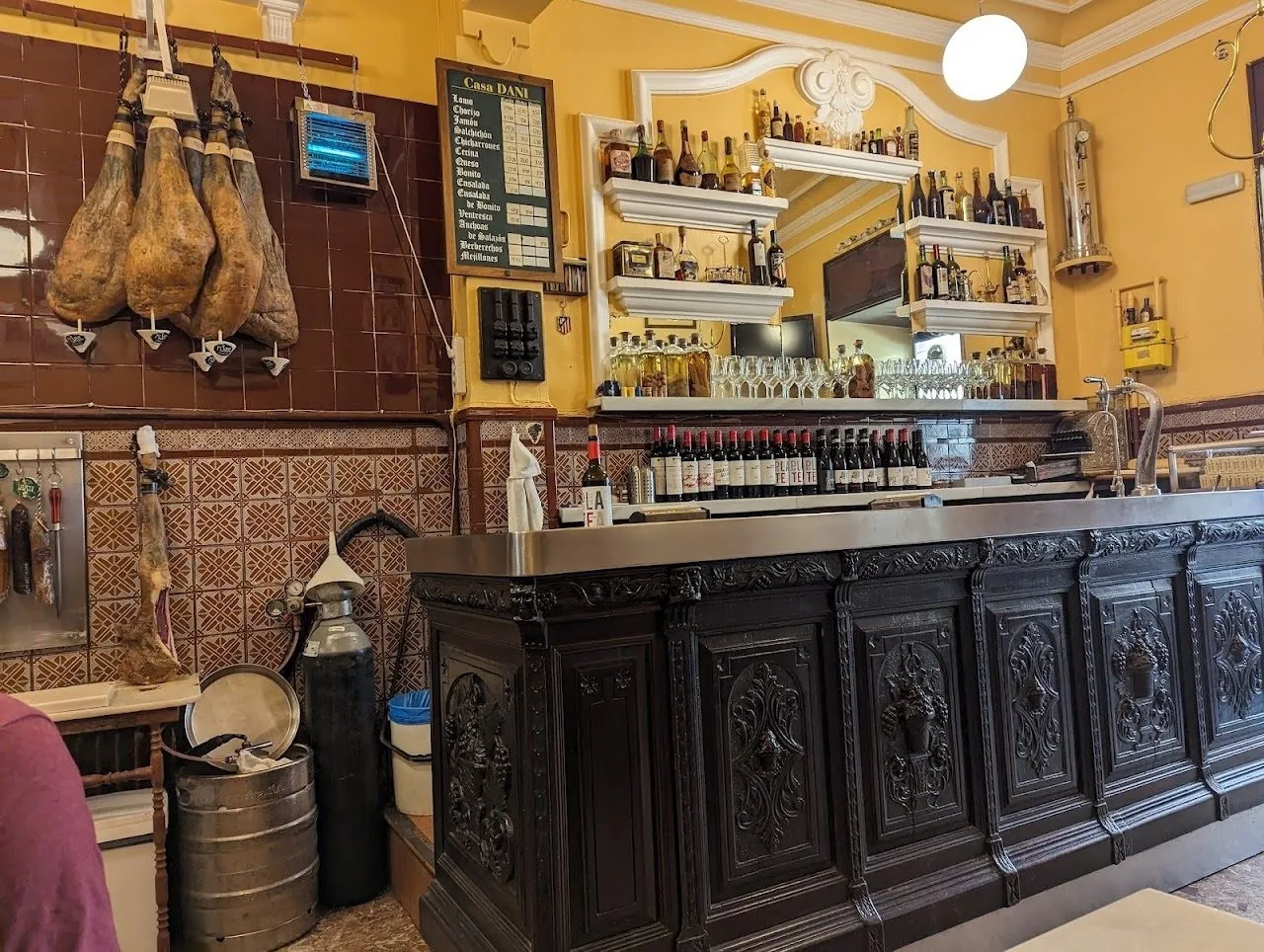 A tiled bar with a dark carved wooden counter and hams hanging above it