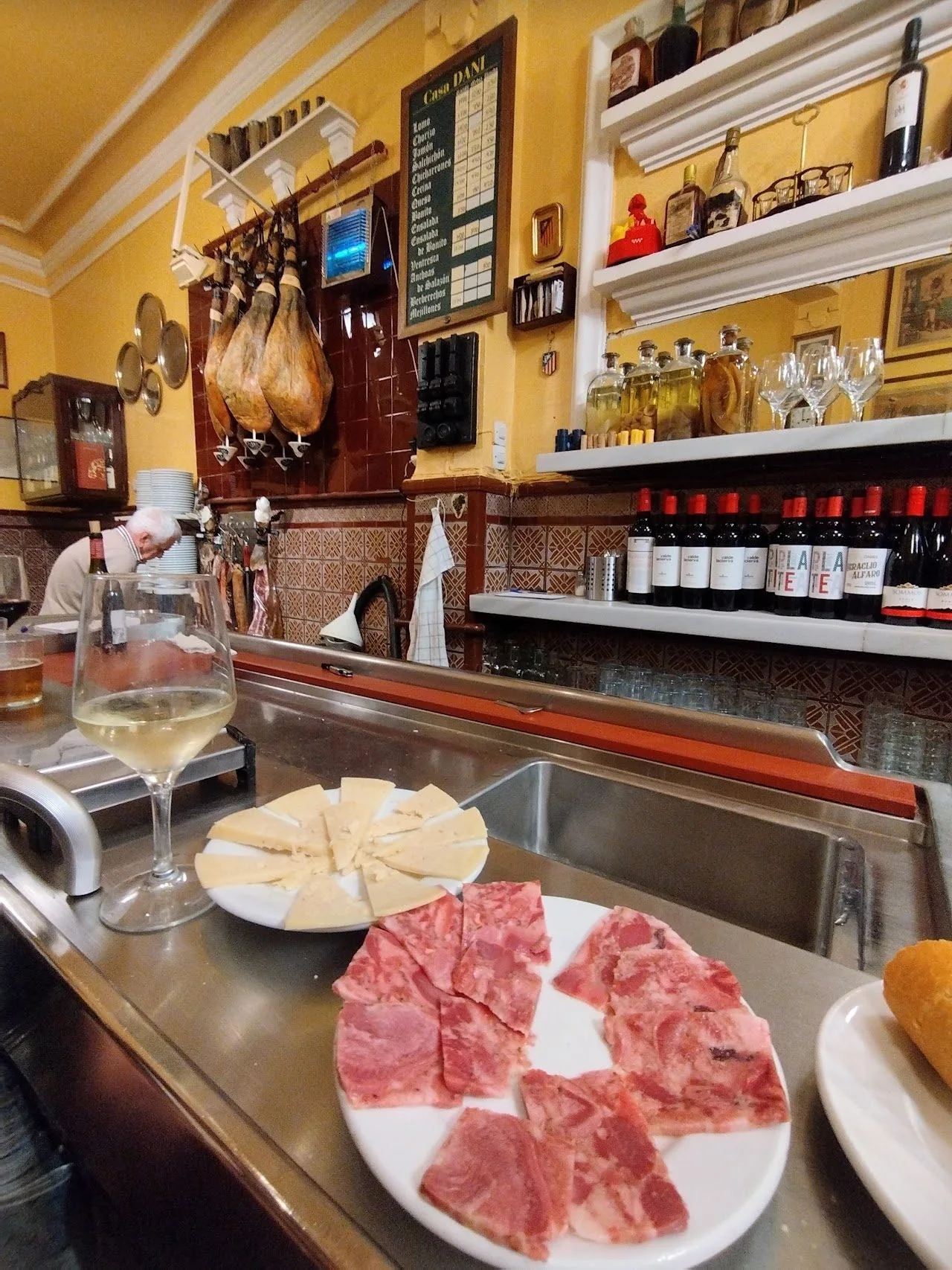 A bar counter with hams hanging behind it and a plate of cured ham slices