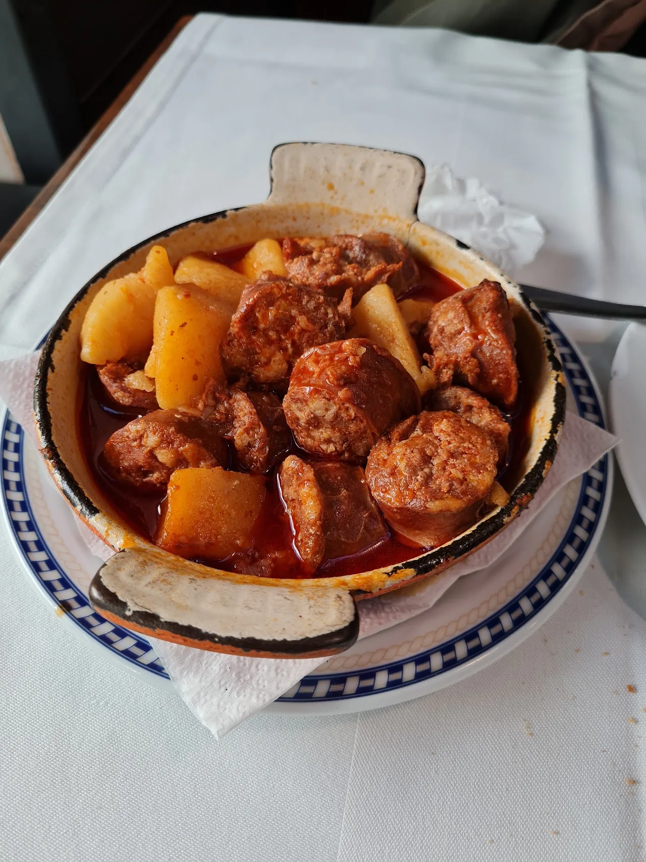 A terracotta dish of stewed sausage and potatoes in a rich sauce