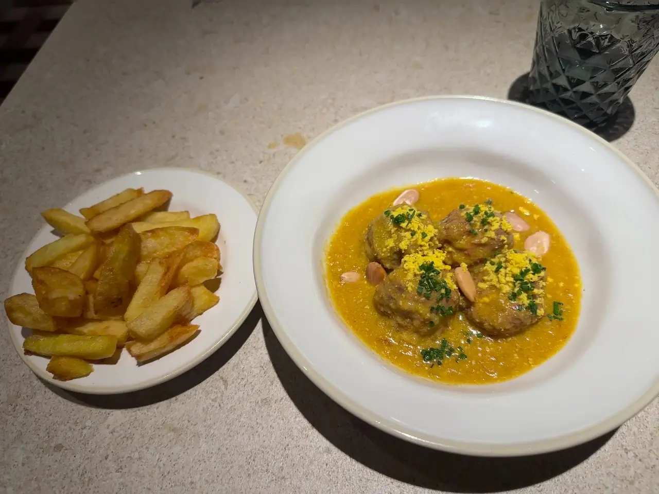 Meatballs in a saffron-colored sauce served with a side of fried potatoes
