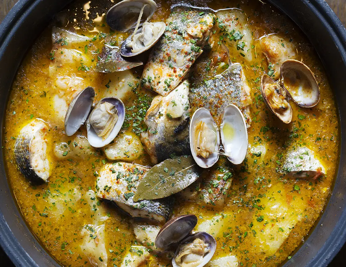 Fish stew with clams, potatoes, and bay leaf in a saffron broth, served in a clay pot at Casa Delfín