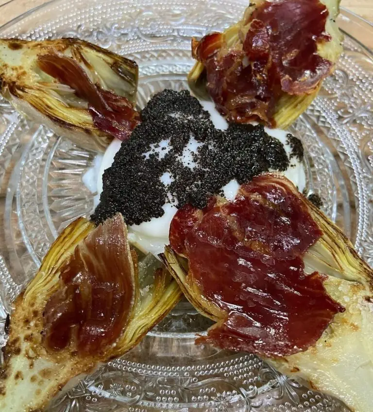 Roasted artichoke halves arranged around a mound of black roe over white cream, topped with crisp jamon, on a pressed-glass plate