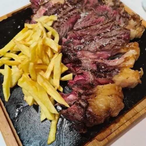 Sliced grilled ribeye steak with flaky sea salt beside a pile of thin fries on a black slate board