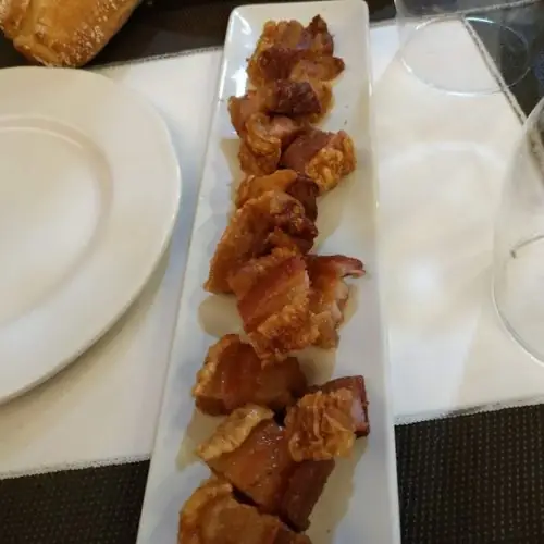 Fried crisp pork belly cubes (torreznos) arranged on a long white plate on a set table