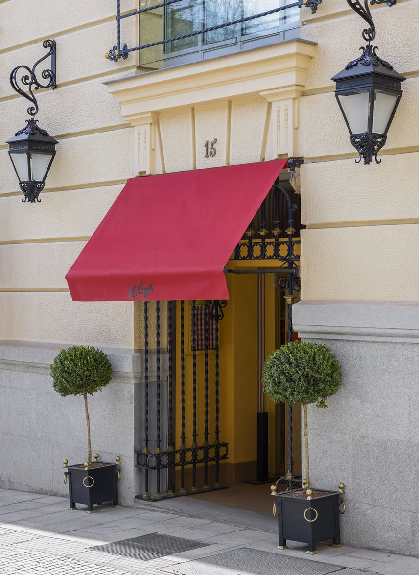 Street entrance under a red awning lettered Felisa, with wrought-iron lanterns either side, two clipped box topiaries in planters and a yellow-painted doorway at number 15