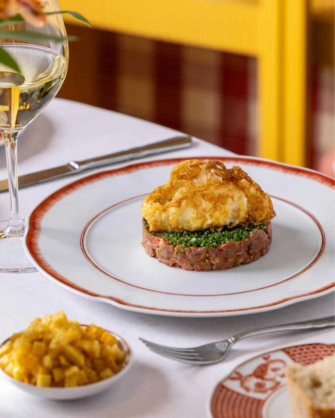 A round stack of chopped topping on a red-rimmed white plate with a small dish of sweetcorn