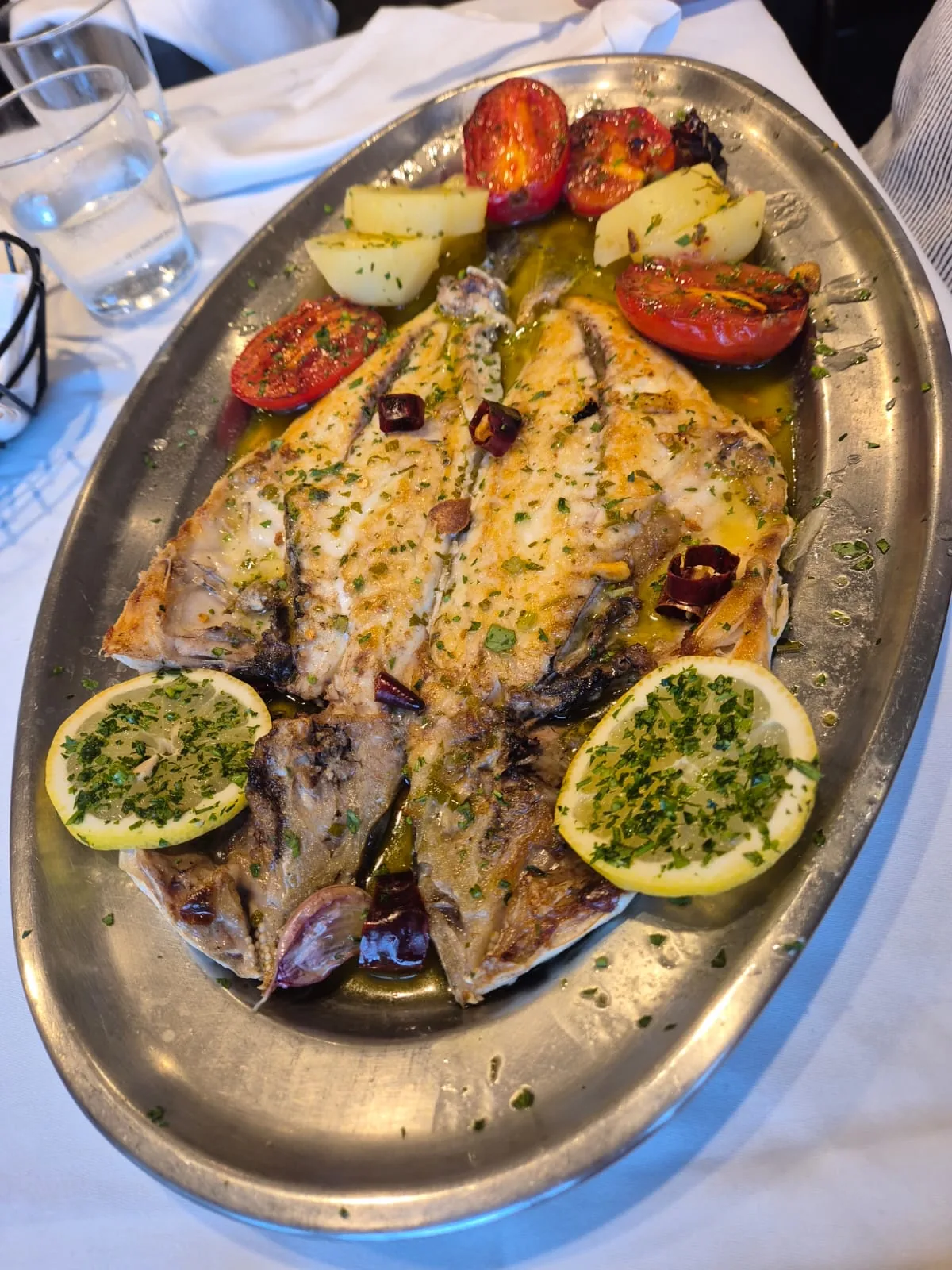 A whole grilled fish topped with garlic and parsley, served with roasted tomatoes and lemon