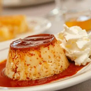 A flan topped with caramel sauce beside a dollop of whipped cream