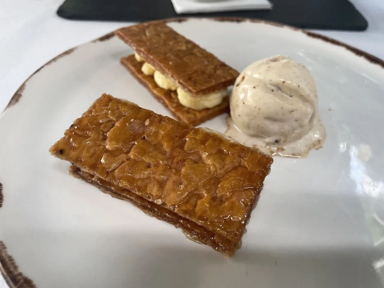 Two thin golden pastry slices with cream and a scoop of ice cream on a plate