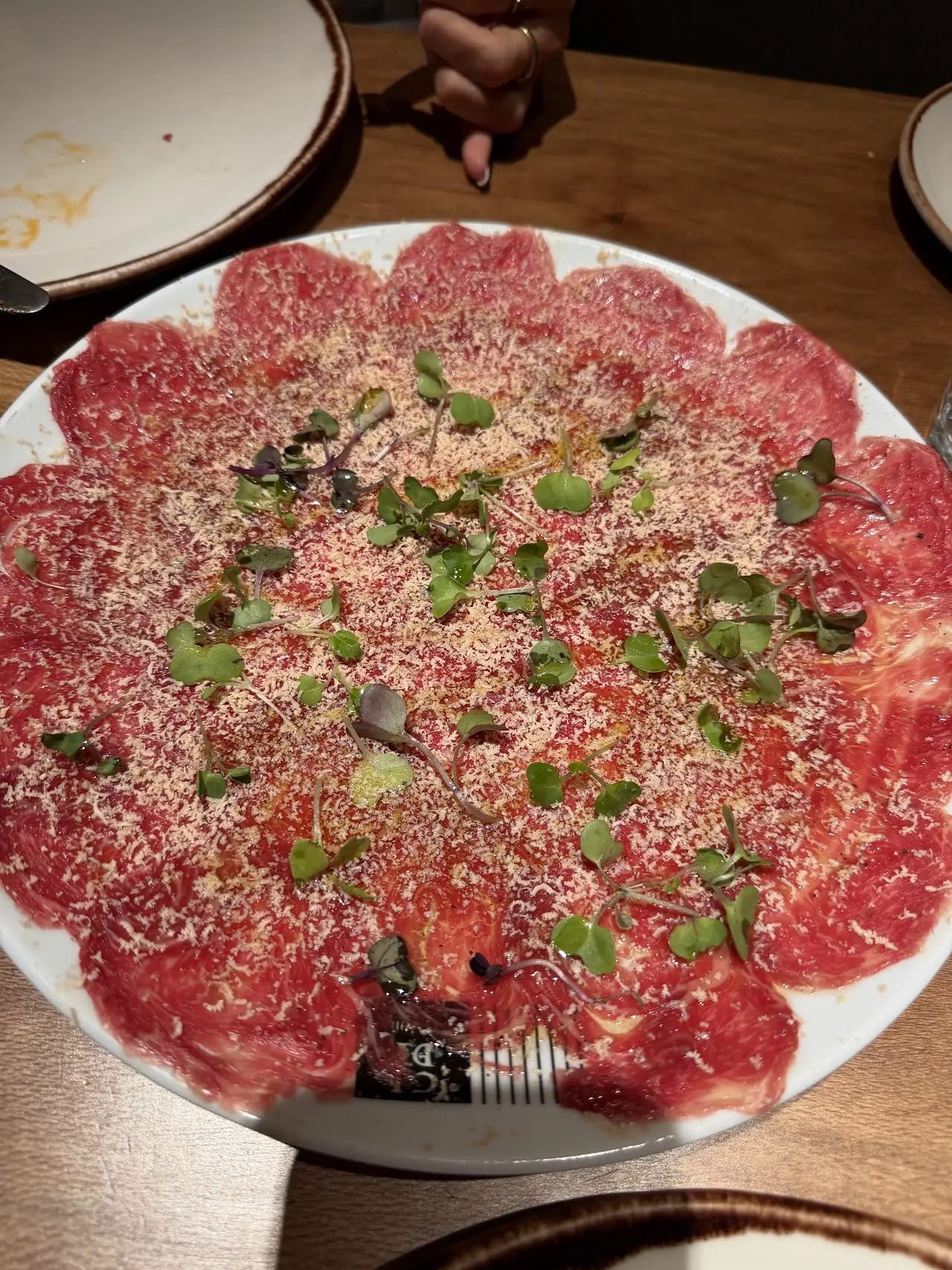 Thin slices of raw beef carpaccio topped with shaved cheese and herbs.