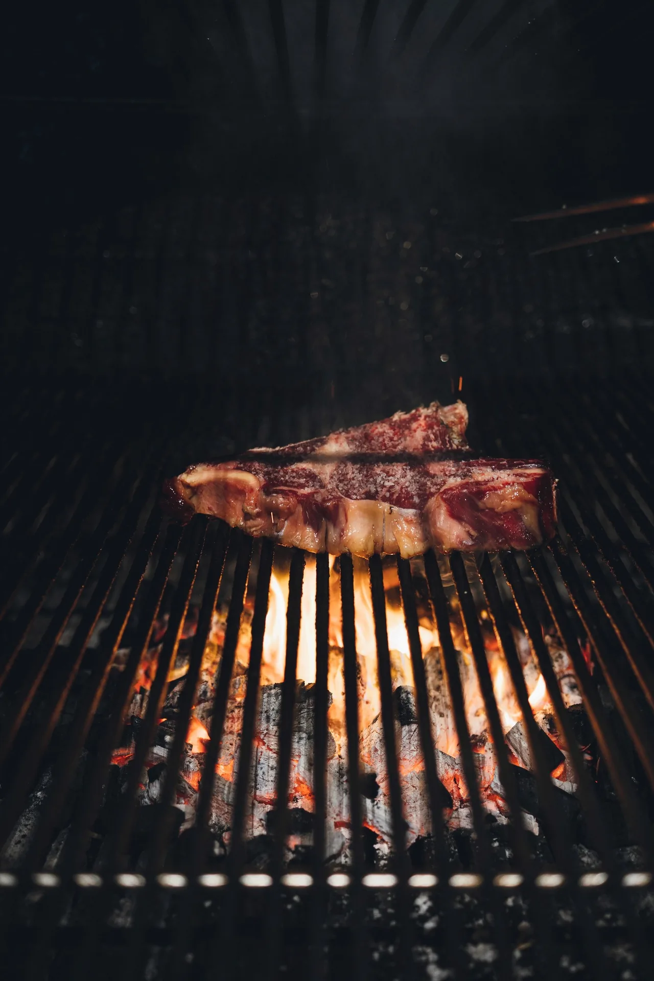 A thick steak cooking on a charcoal grill against a dark background