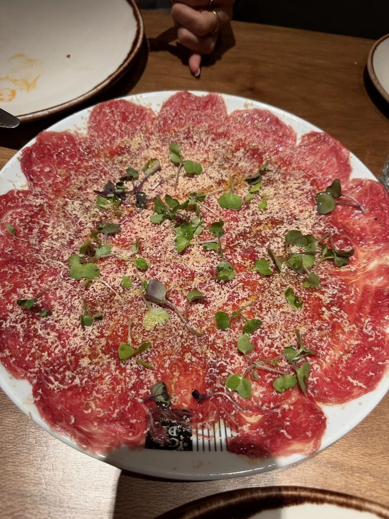 A plate of thinly sliced raw beef carpaccio topped with herbs and shavings