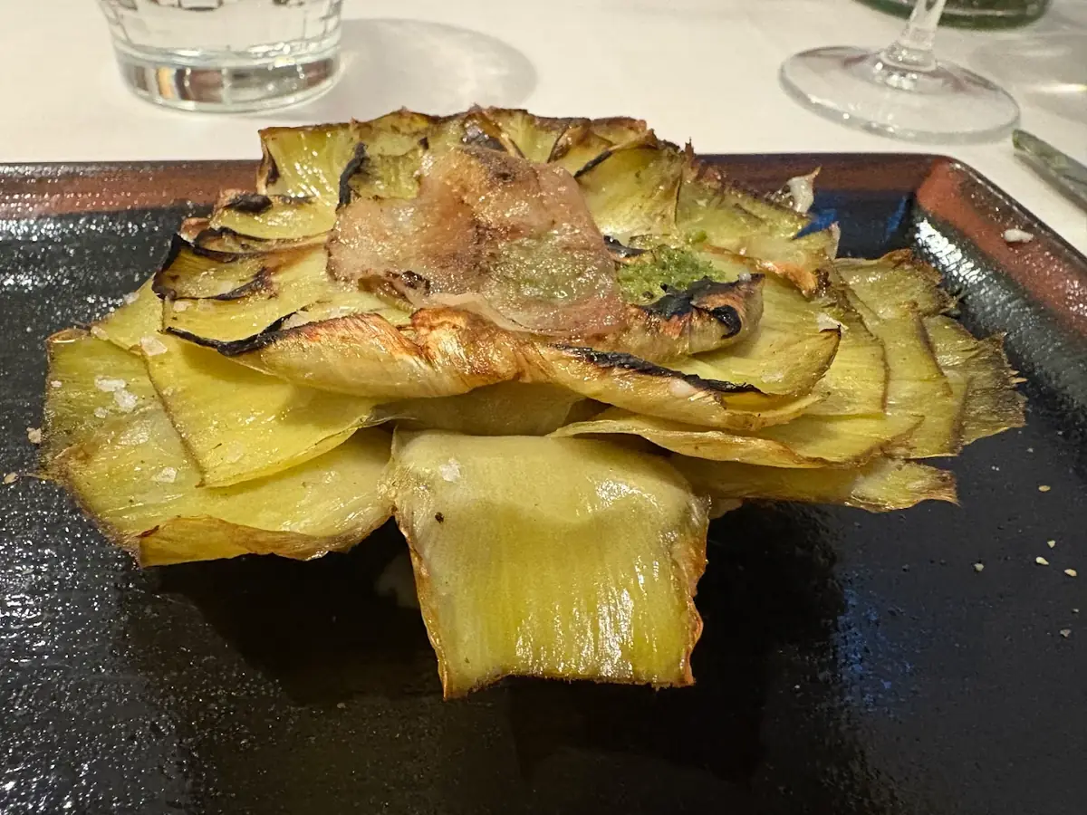 Grilled artichoke leaves arranged in a flower shape on a dark tray.