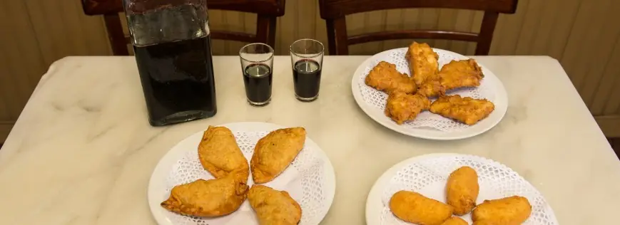 Plates of fried croquettes and pastries on a marble table with two small glasses of dark wine