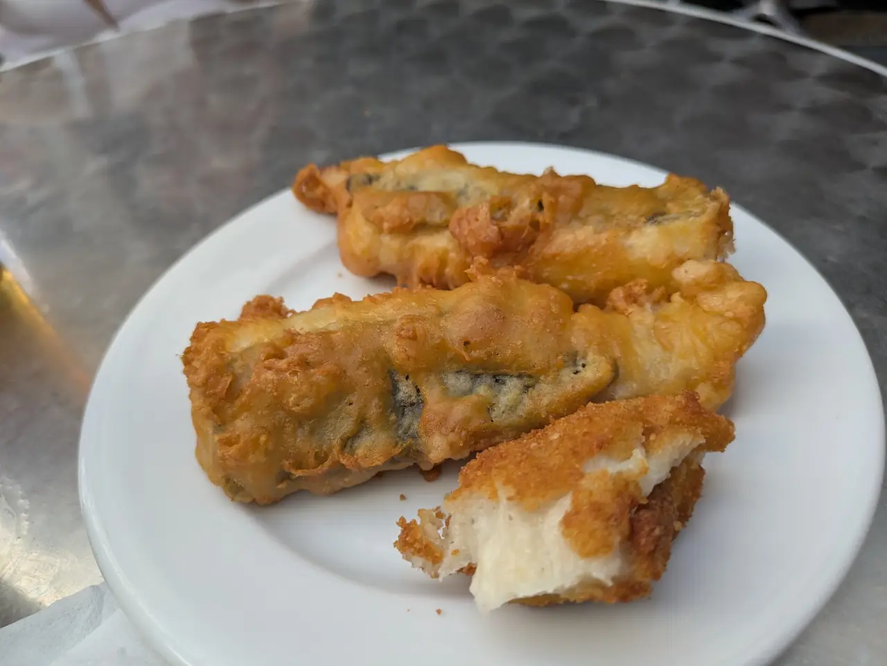 Battered fried cod pieces on a white plate at the bar counter