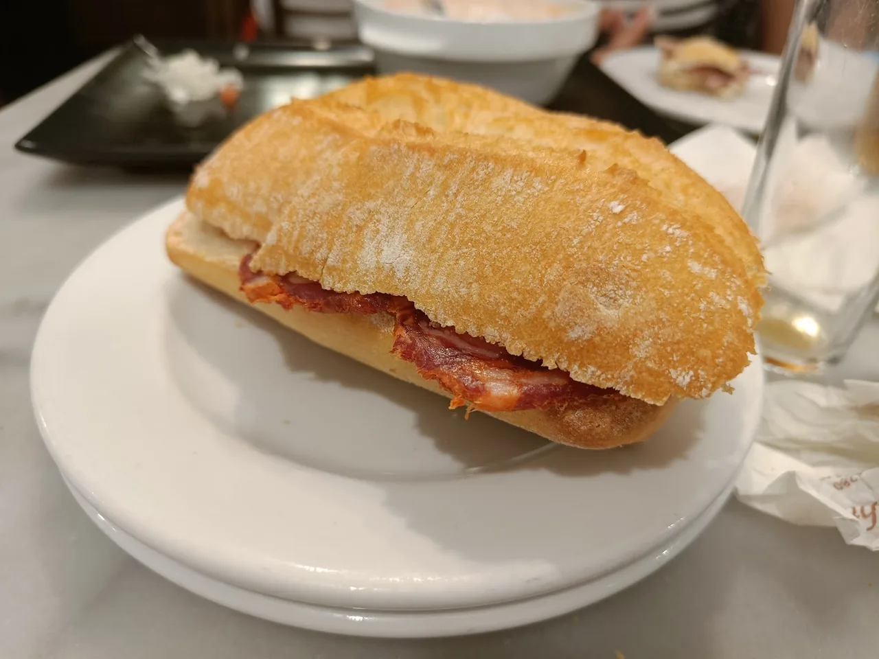 A small crusty bread roll filled with cured meat on a white plate