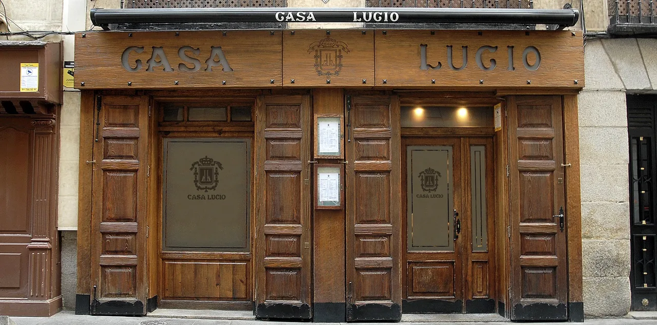 A dark wooden restaurant facade with a carved sign above two panelled doors