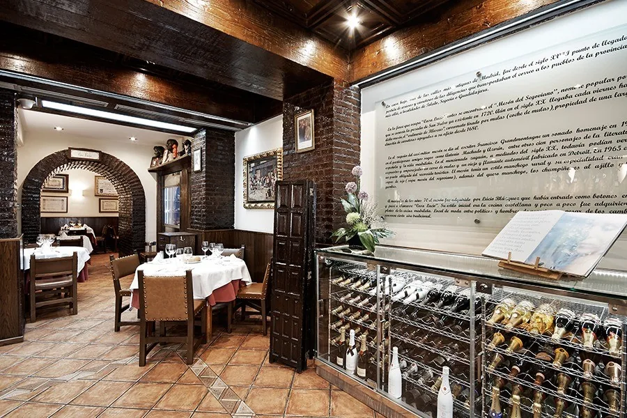 A dining room with brick arches, dark wooden chairs, white-clothed tables and a wine display