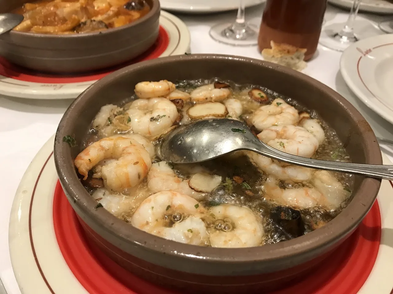 A terracotta dish of prawns in oil and garlic with a spoon