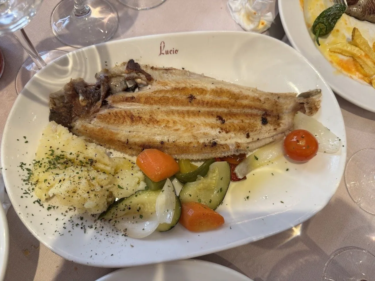 A whole grilled flatfish served with potatoes and vegetables on a white plate.