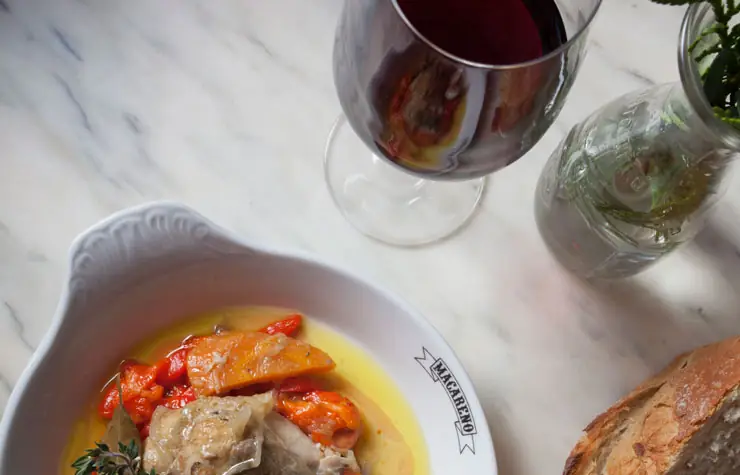 Bowl of roasted red peppers and cod in olive oil in a branded Macareno dish, with red wine and bread