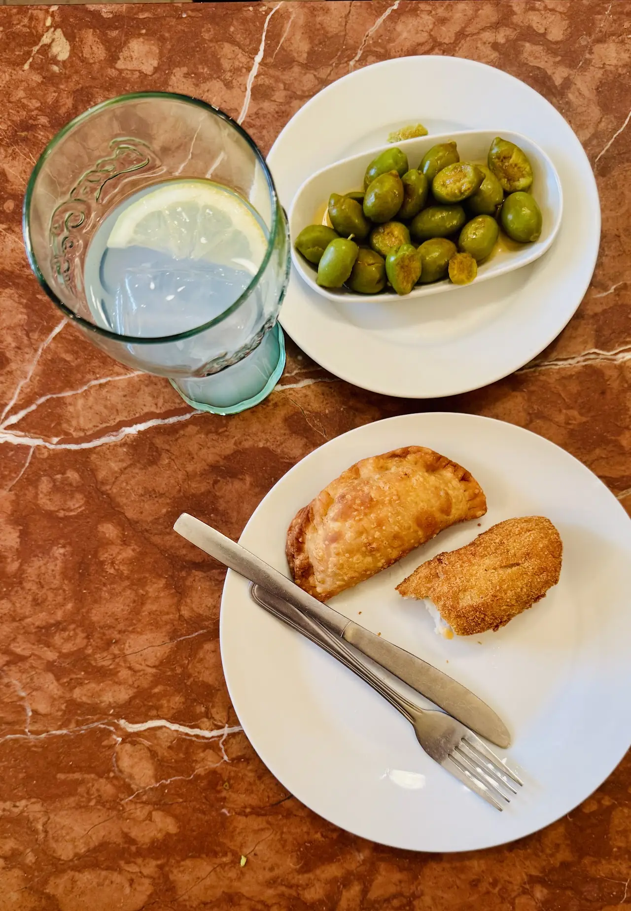 Empanadillas and a dish of green olives on a marble table