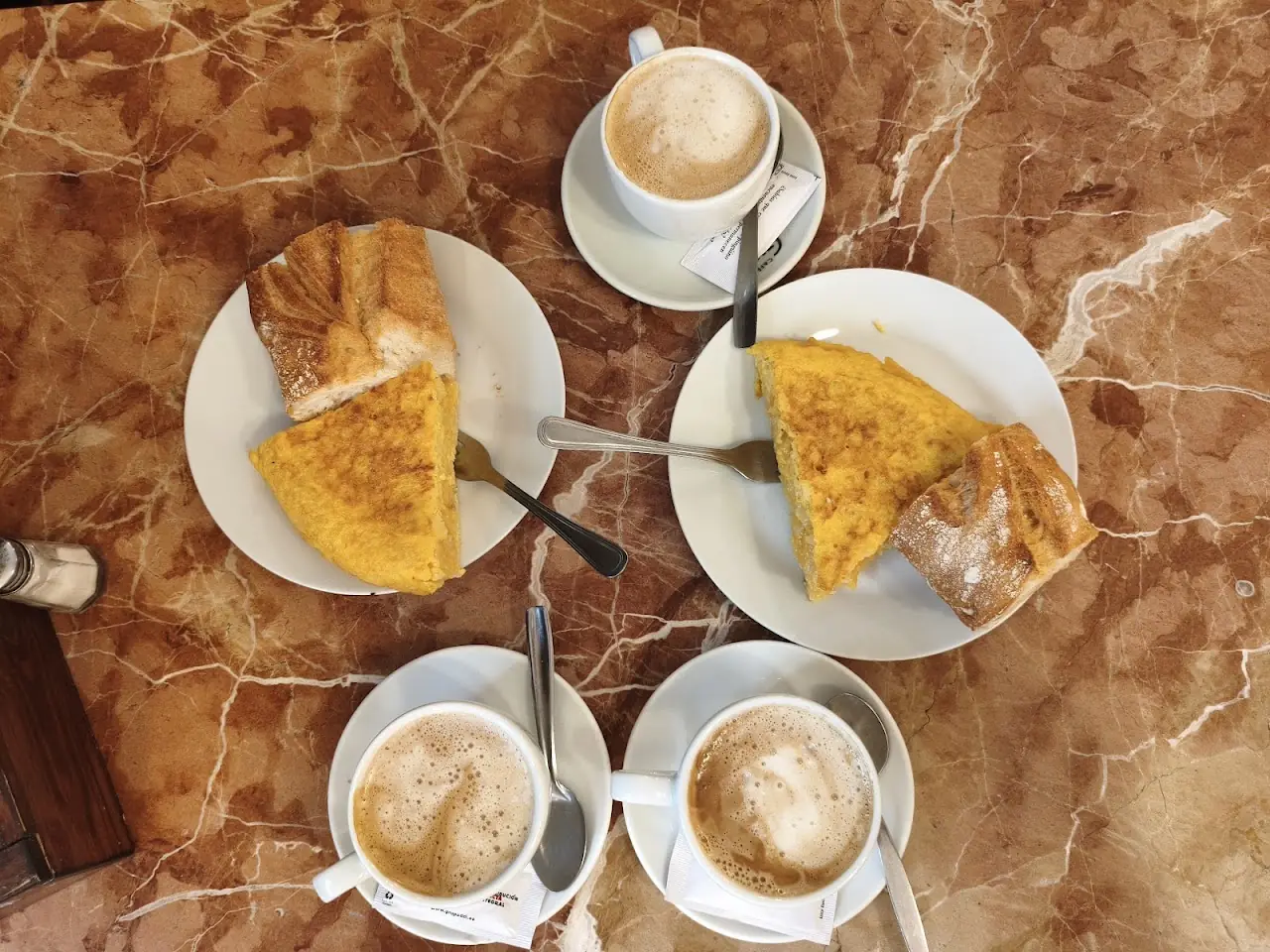 Slices of tortilla de patata with café con leche on a marble table