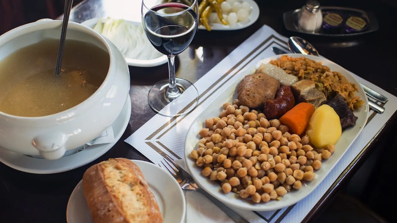 A bowl of broth soup next to a plate of chickpeas and vegetables