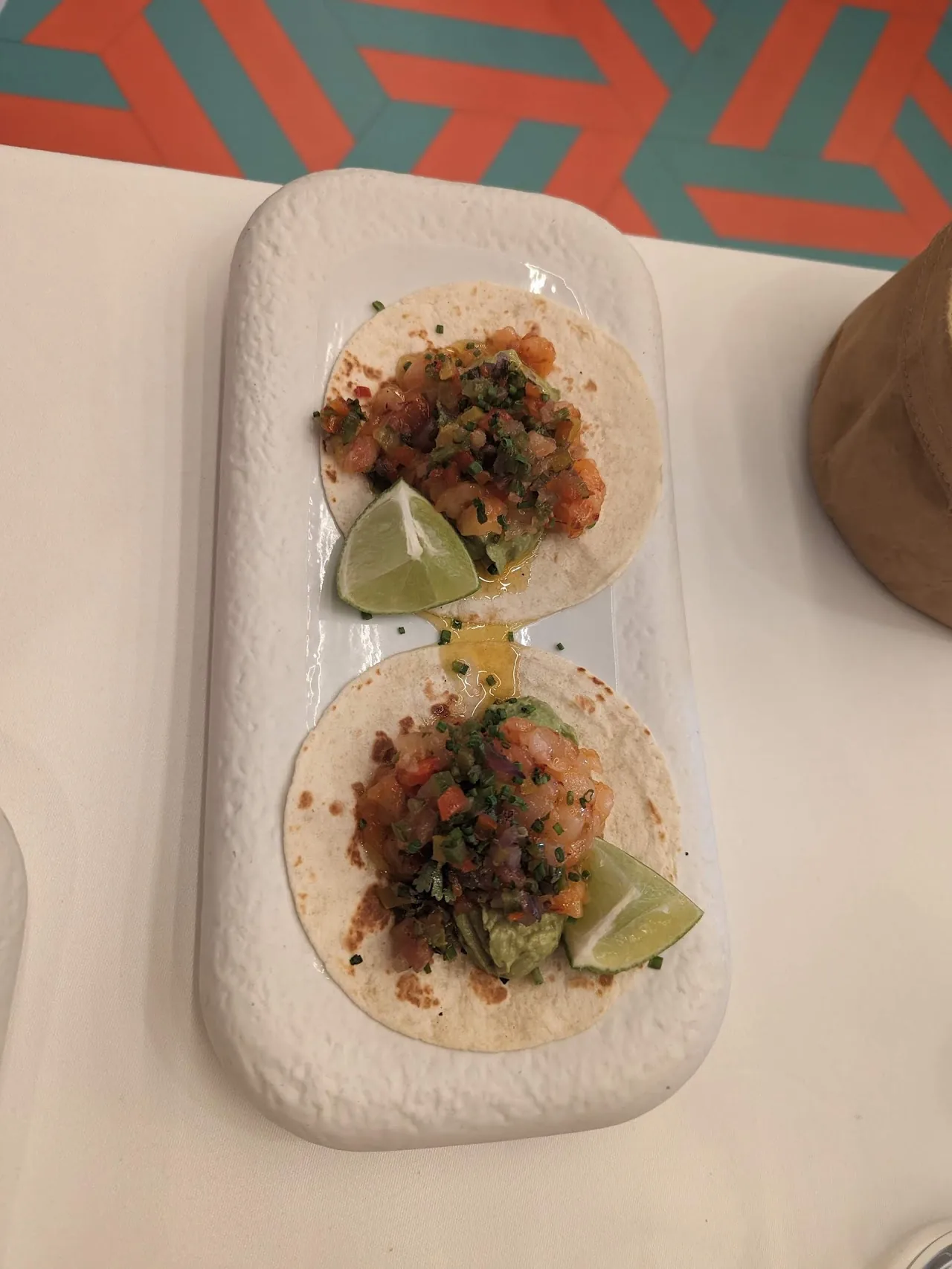 Two tacos topped with diced tomato and cilantro, served with lime wedges
