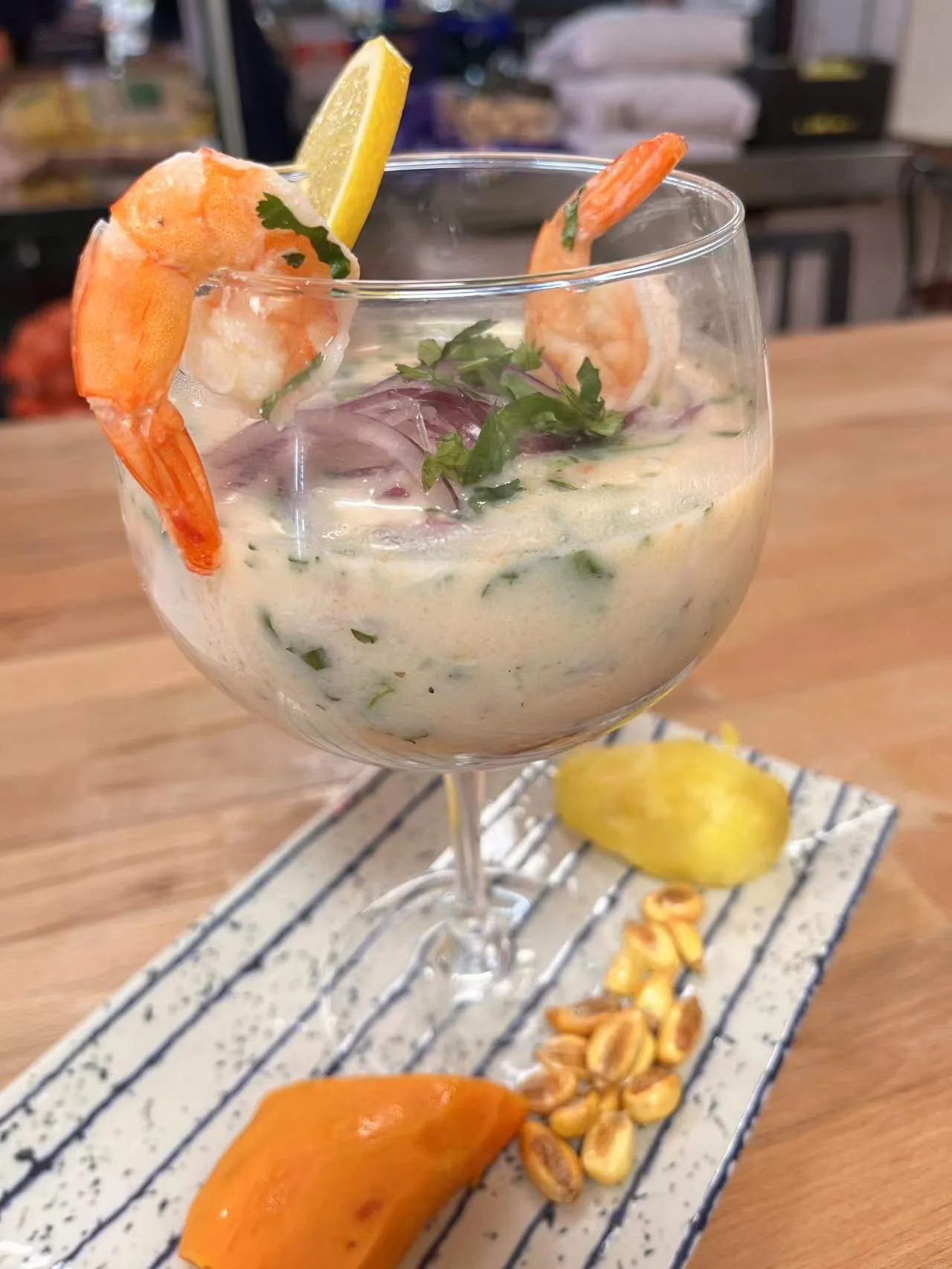 A glass of shrimp ceviche garnished with herbs and a lemon wedge