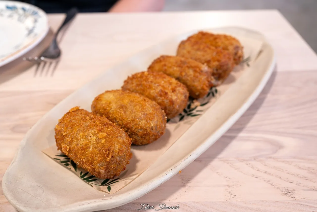 A row of five golden breaded croquetas on a long cream plate