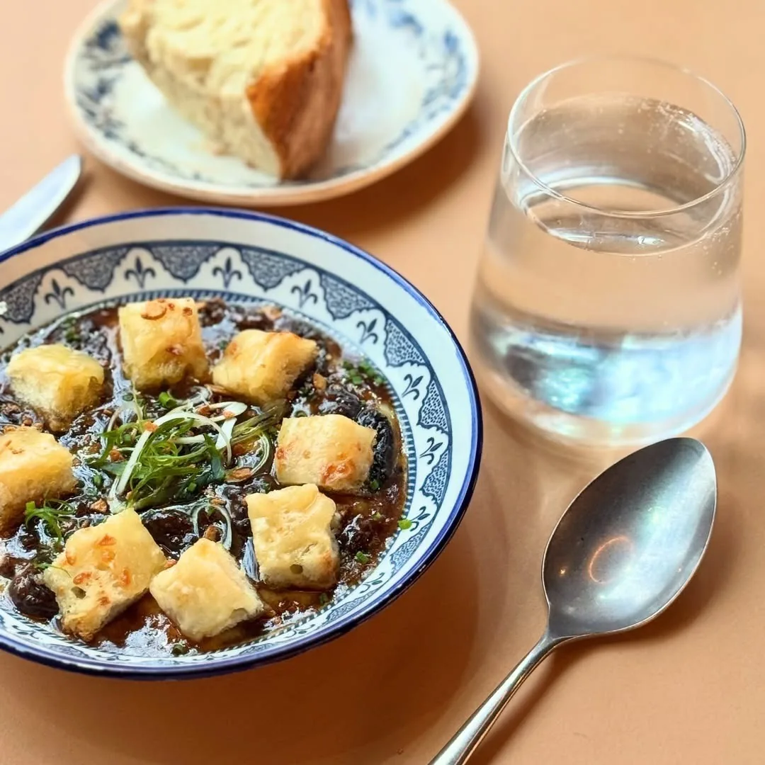 A blue and white bowl of a dark stew with golden cubes and green leaves beside a glass of water