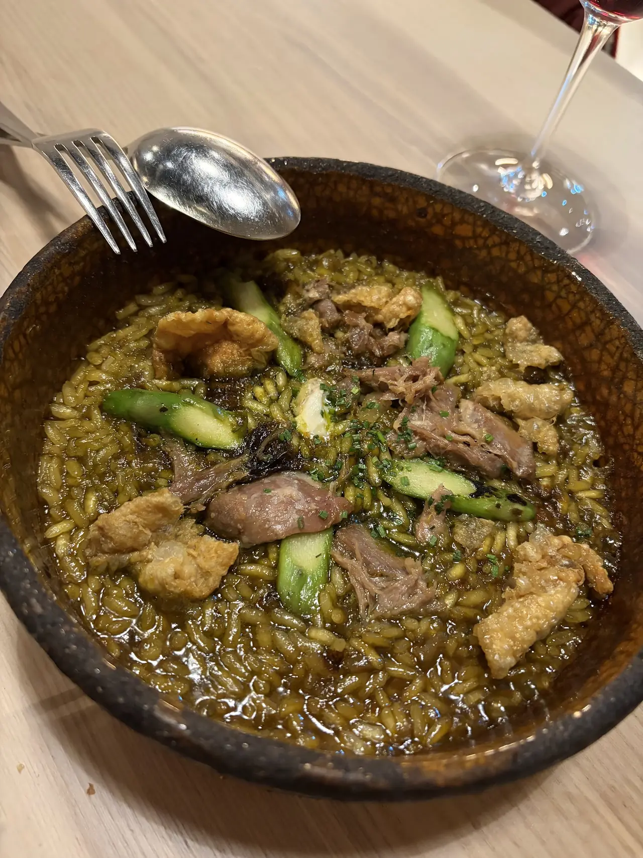Rice dish in a clay pan with shredded meat, crispy skin, green asparagus and chives