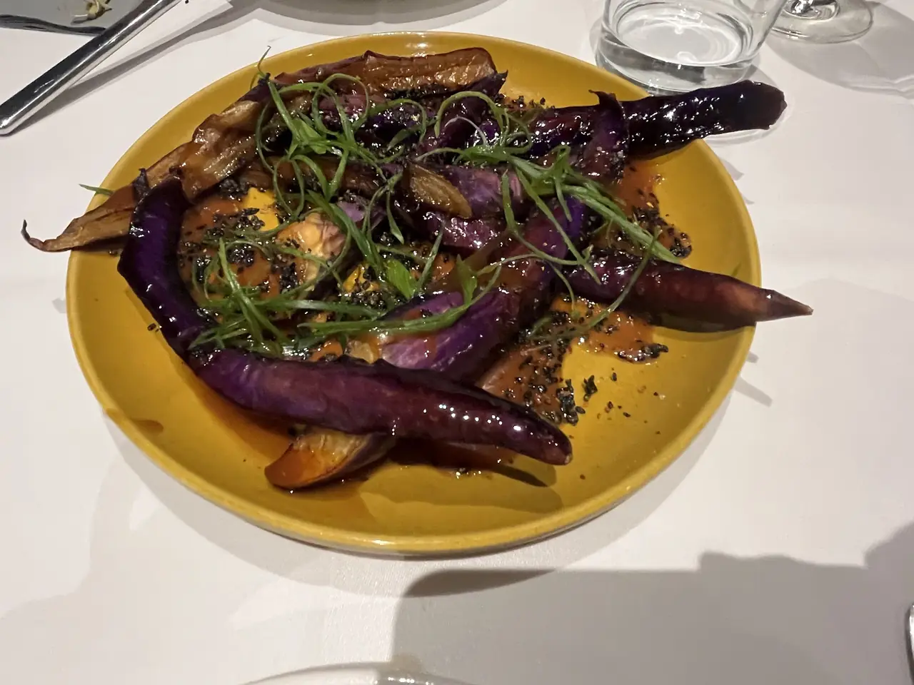 Roasted purple eggplant halves glazed in sauce with scallion and sesame on a yellow plate
