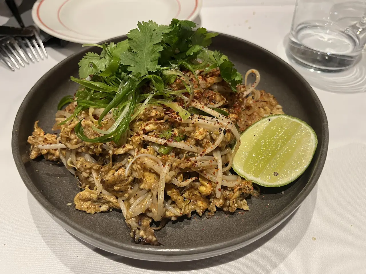 Stir-fried noodles with bean sprouts, egg, herbs and a lime wedge on a dark plate