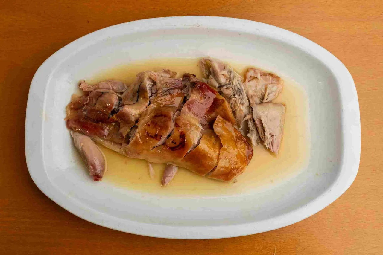 An oval white plate of roast meat in juices, seen from above on an orange table