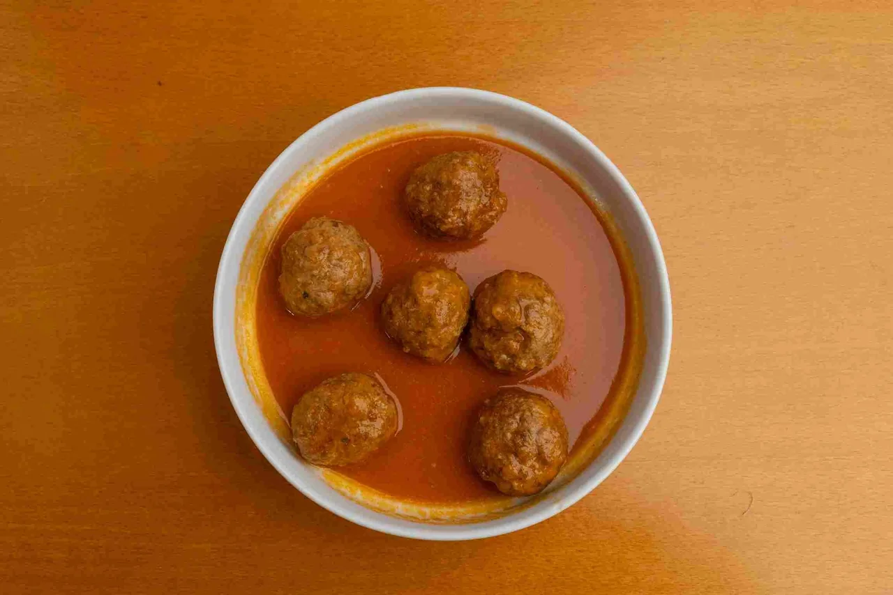 A white bowl of meatballs in sauce on an orange table