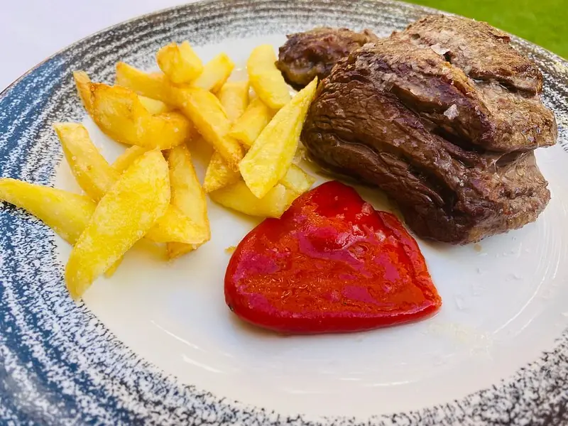 Grilled steak with fried potatoes and a roasted red pepper.