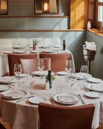 Round tables set with wine glasses and napkins in a wood-trimmed dining room