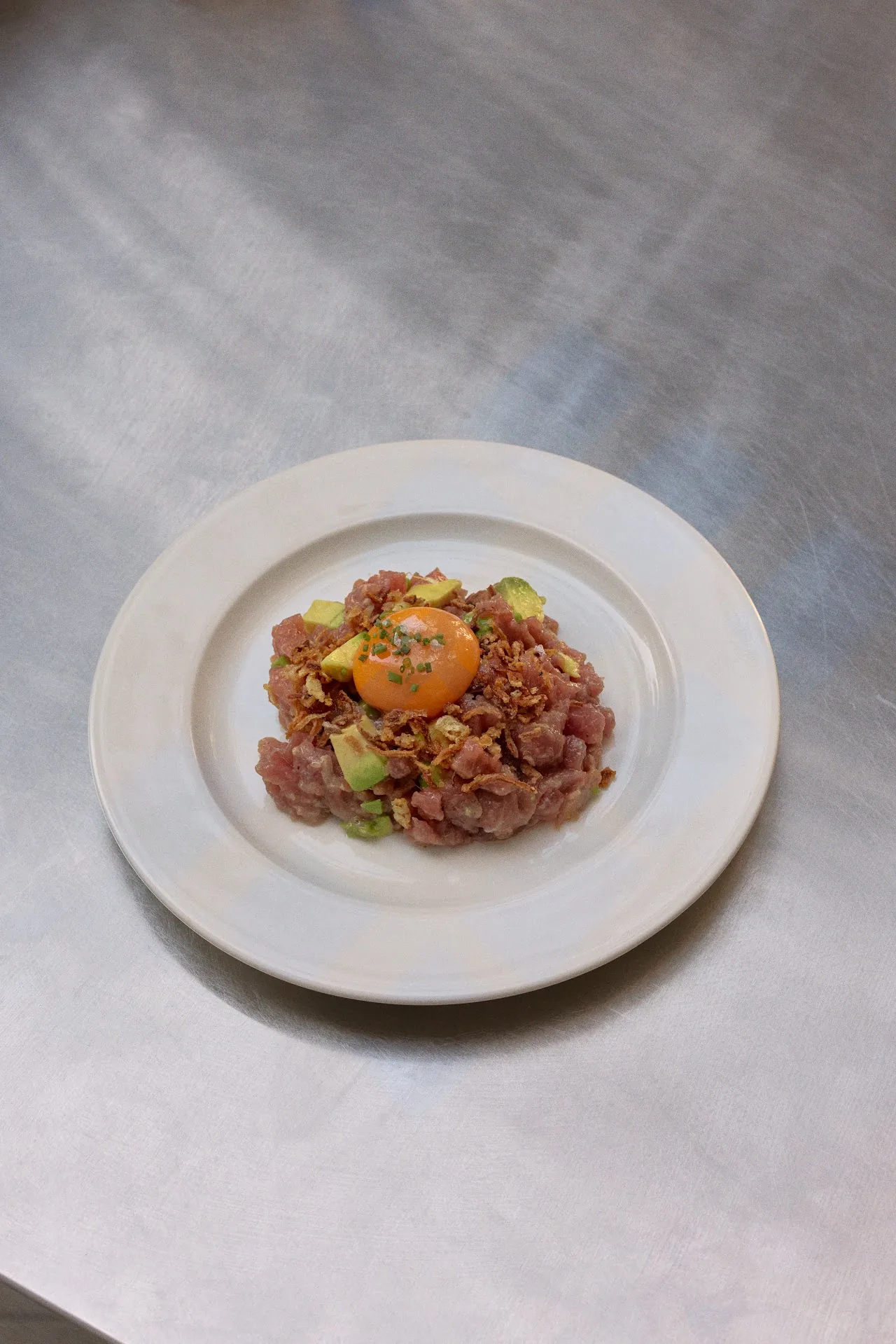 A small plate of tartare with diced tomato and greens, seen from above